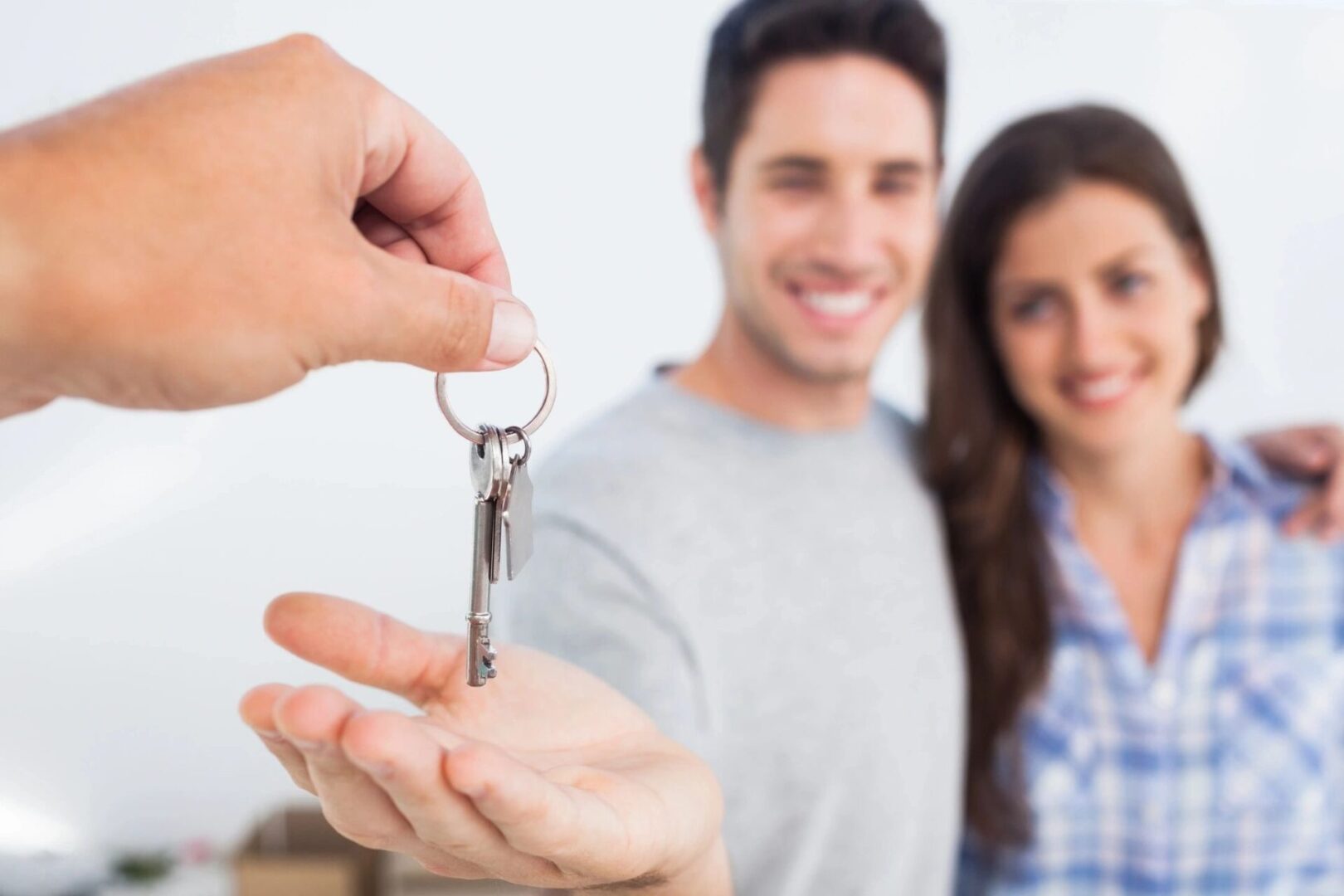 A couple being handed over a key of the house with them smiling
